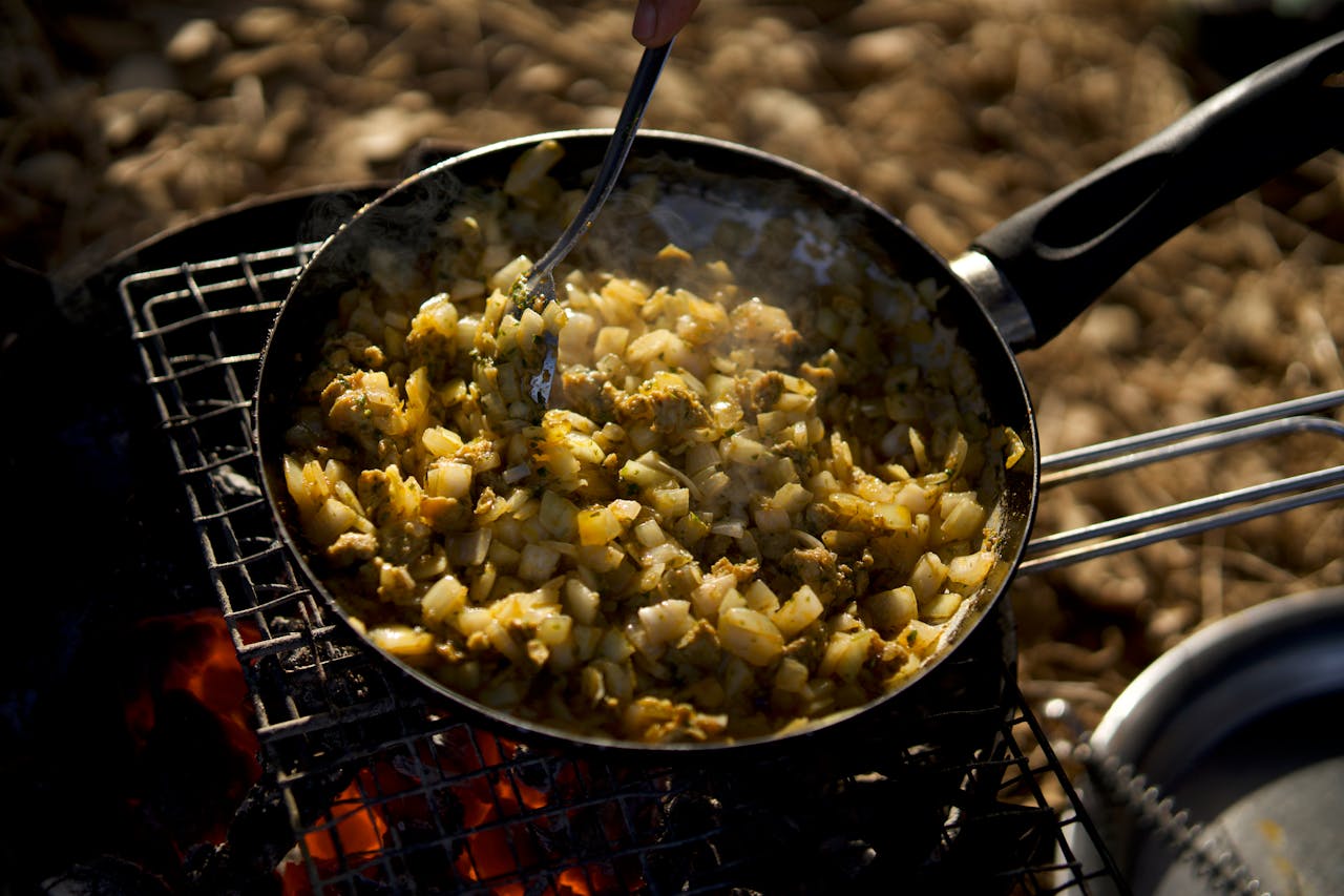 Home Close-up of a skillet with vegetables being cooked outdoors over an open flame.